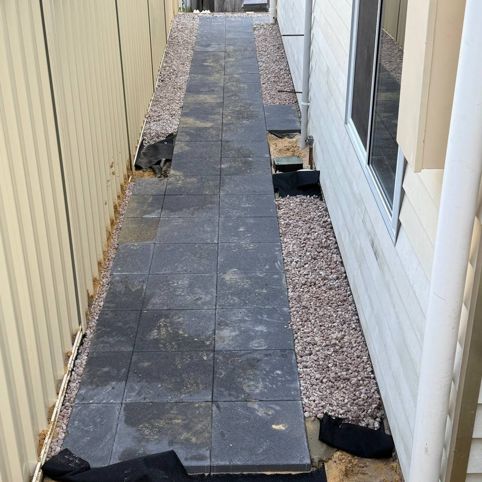 Side path of large charcoal pavers with decorative gravel borders beside a cream Colorbond fence