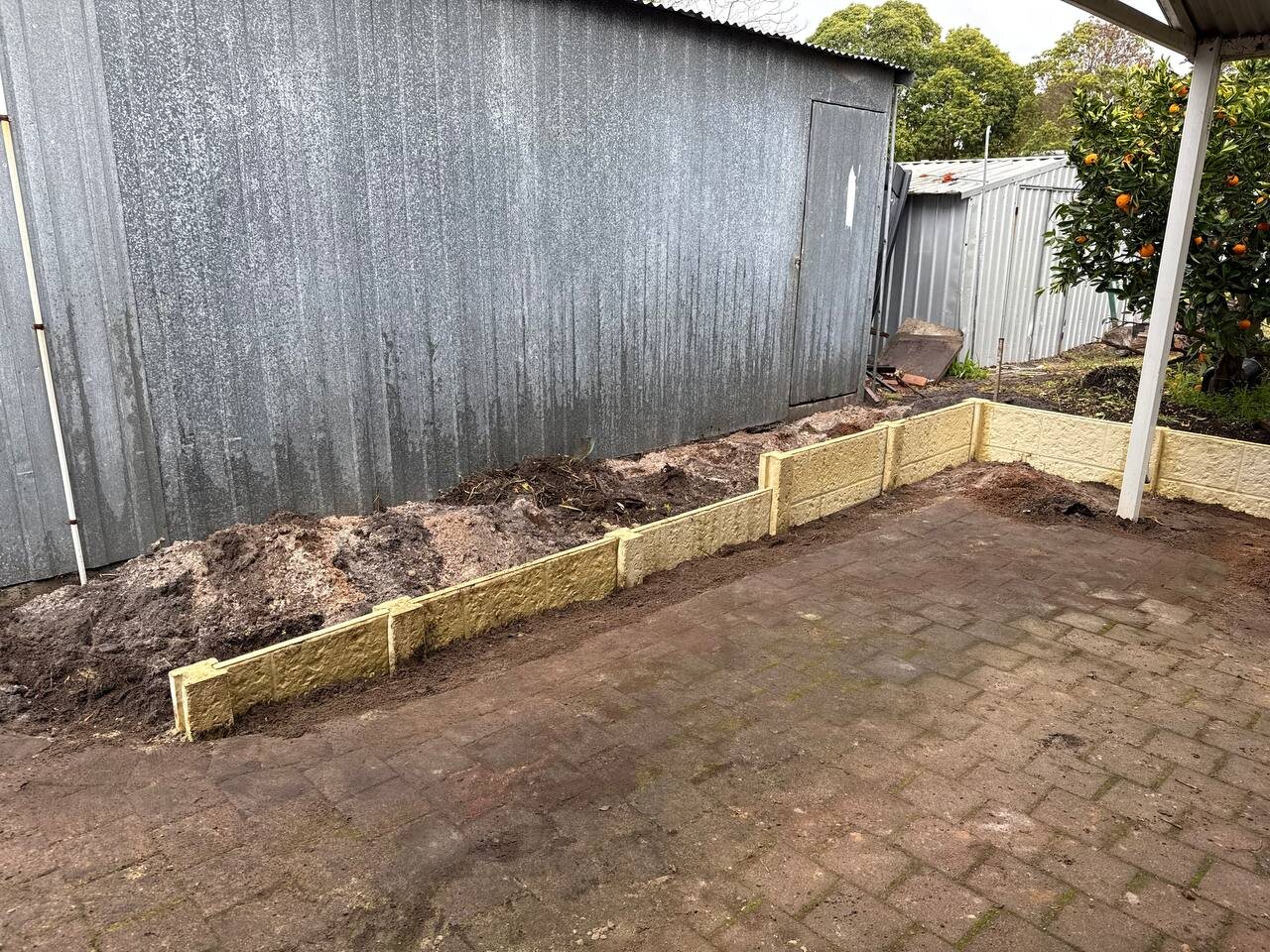 Twin-sided limestone retaining wall beside a shed
